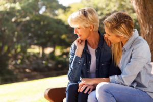 an adult child sits with their elderly parent under a tree possibly recognizing signs of dementia