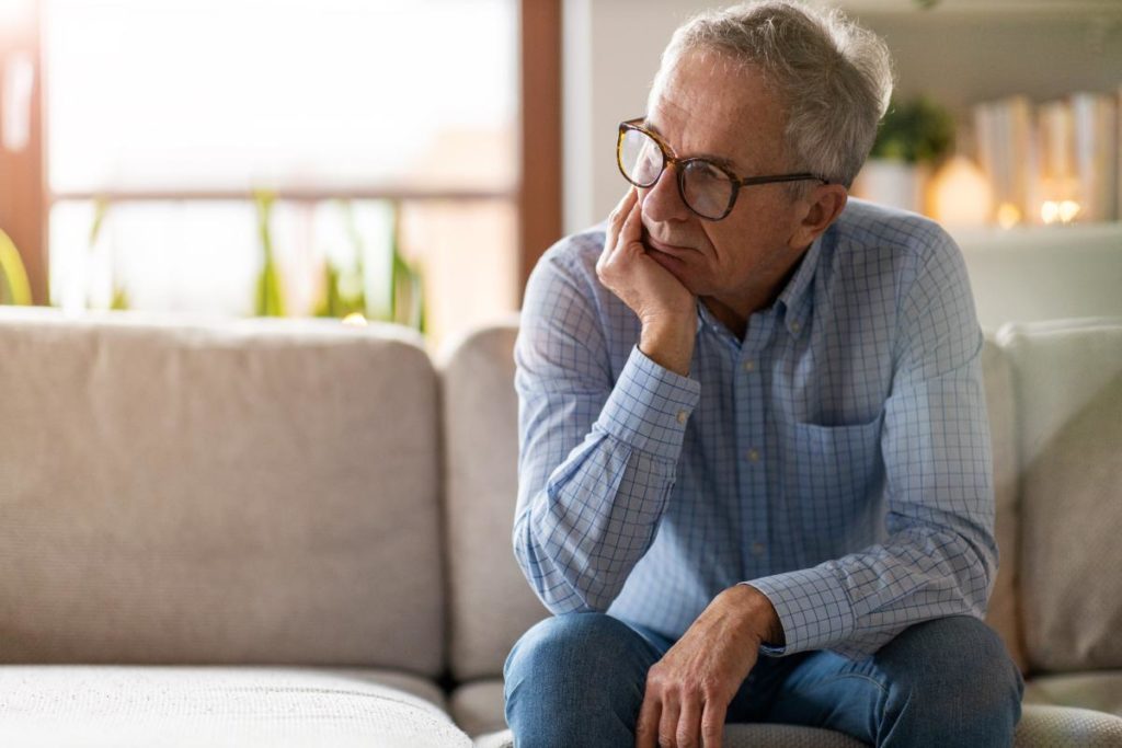 an elderly person sits on a couch possibly pondering the difference between alzheimer's vs dementia
