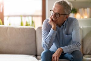 an elderly person sits on a couch possibly pondering the difference between alzheimer's vs dementia
