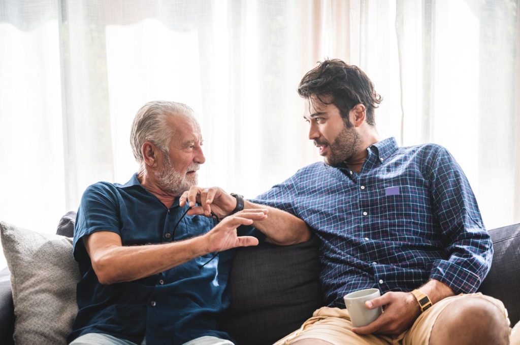an adult child talks with their elderly parent on the couch about seniors giving up their license