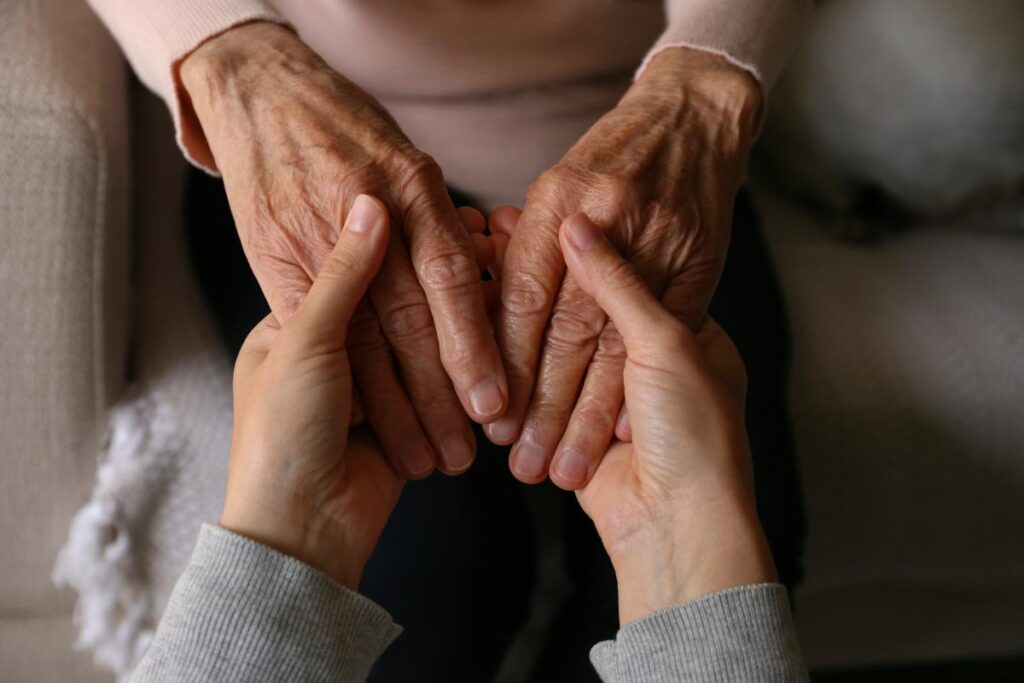caretaker holding hands of older adult reaping the benefits of assisted living